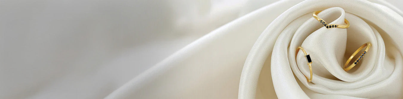 Anillos fino oro amarillo engastados diamantes negros sobre tela blanca sedosa, colección joyería moderna