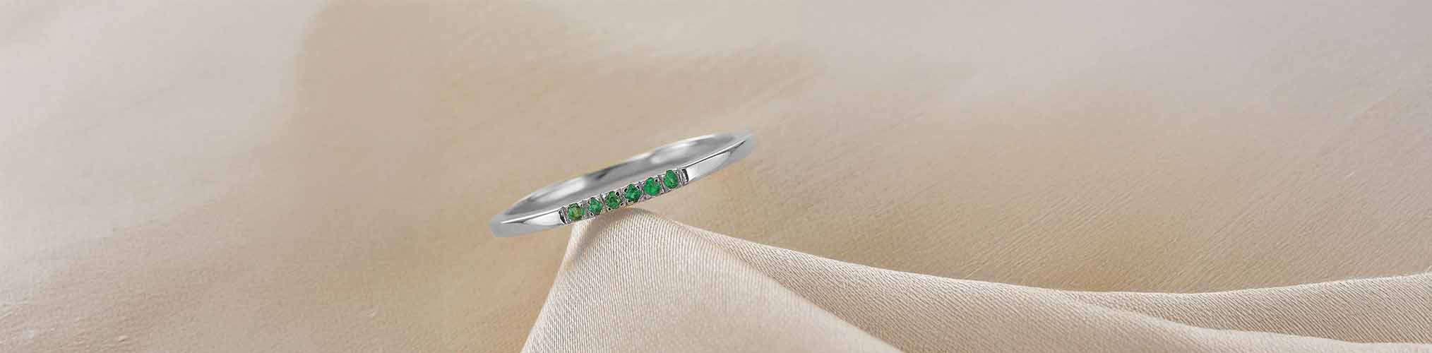 Alianza plata 925 engastada esmeraldas verdes alineadas, anillo fino joyería moderna sobre tela beige
