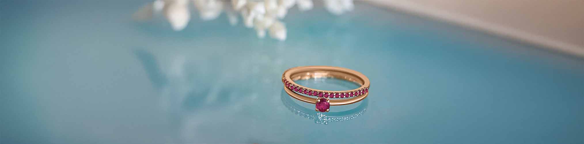 Anillo de compromiso oro rosa engastado rubí con pavé piedras preciosas rojas sobre fondo azul acuático