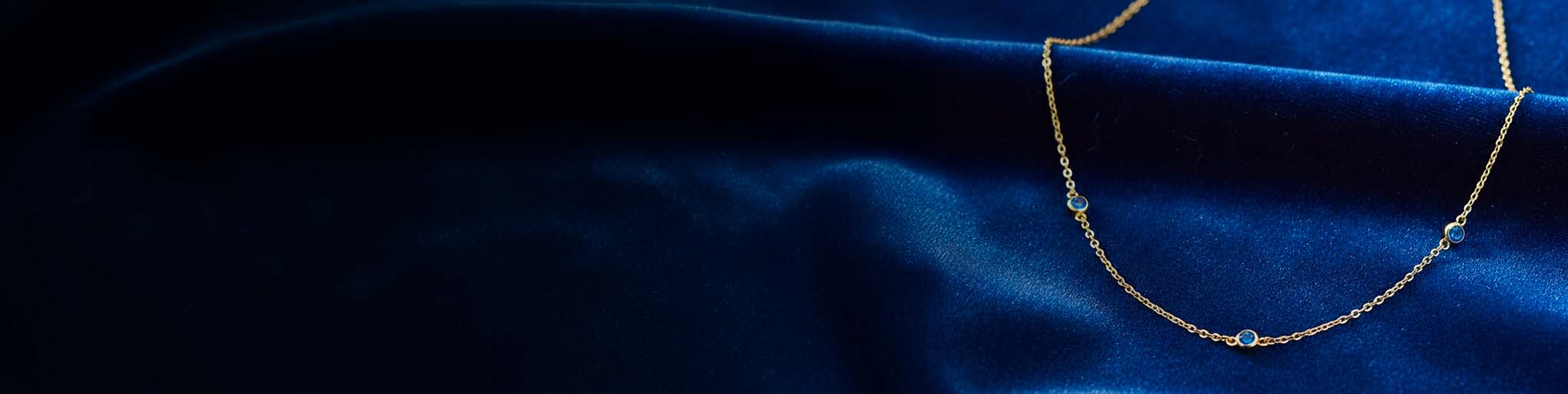 Collar vermeil zafiros azules sobre cadena fina dorada posicionado sobre seda azul marino lujosa joyería francesa