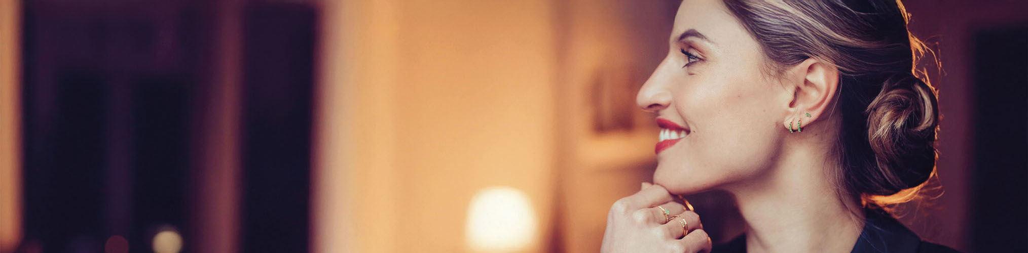 Pendientes oro portados por mujer sonriente de perfil, joyería elegante con reflejos dorados