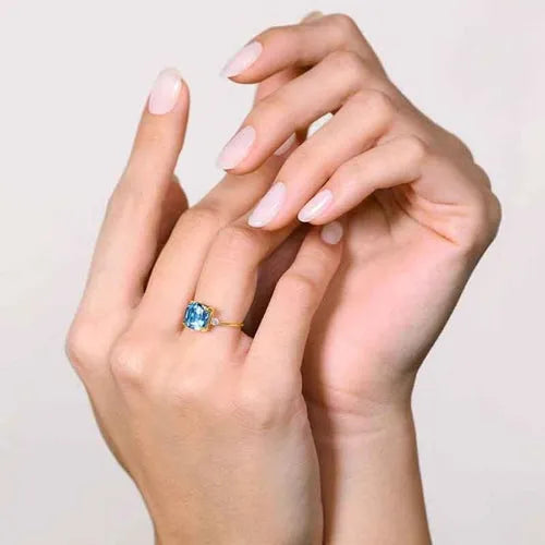Anillo de topacio azul talla cojín en oro amarillo, llevado puesto en las manos