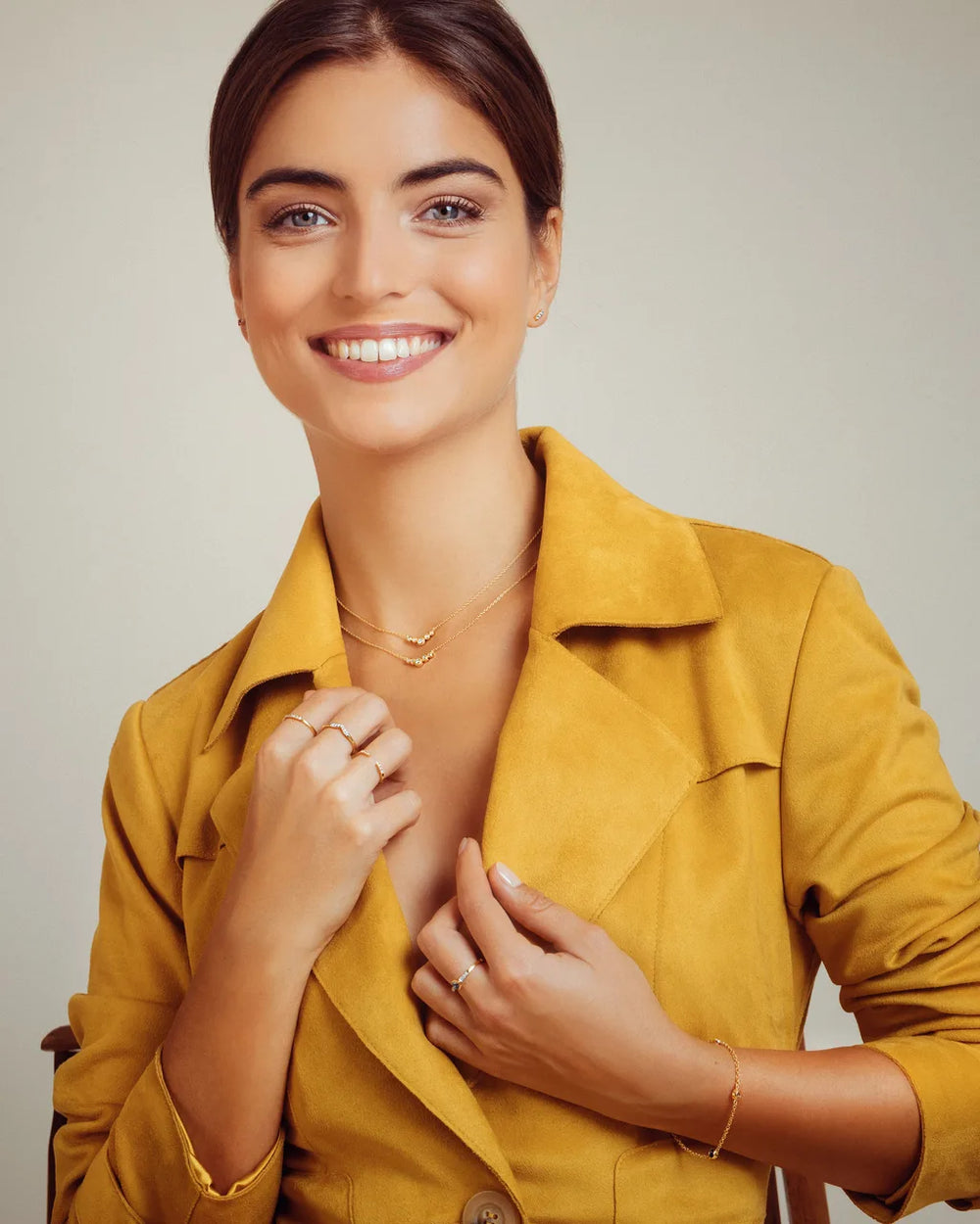 Bagues et bracelet en or jaune portés par une femme en veste ocre sur fond beige Mayuri
