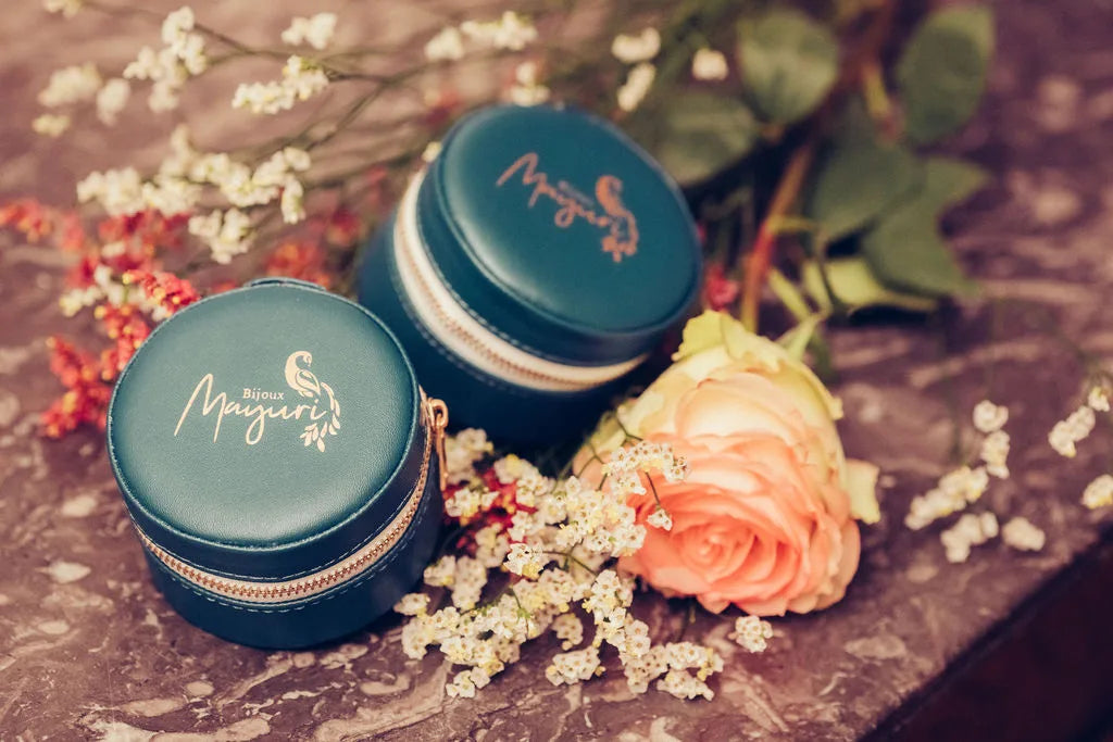 Dos estuches de joyeria redondos Mayuri en terciopelo turquesa sobre fondo lifestyle con flores secas y rosas