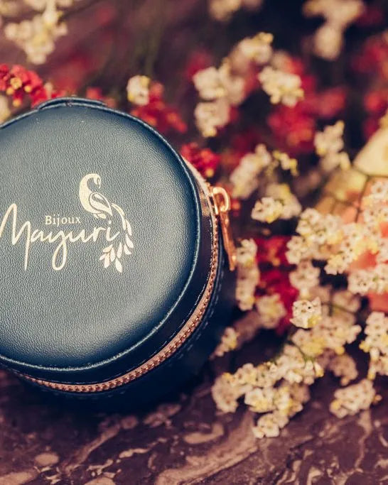 Estuche redondo Mayuri terciopelo turquesa con joyería fina sobre fondo lifestyle floral