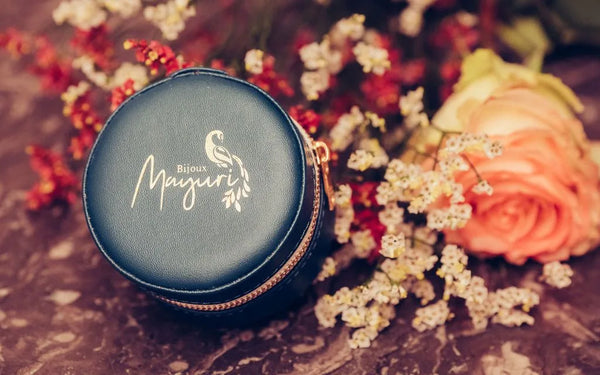 Estuche redondo Mayuri de terciopelo turquesa con joyas finas sobre un fondo floral