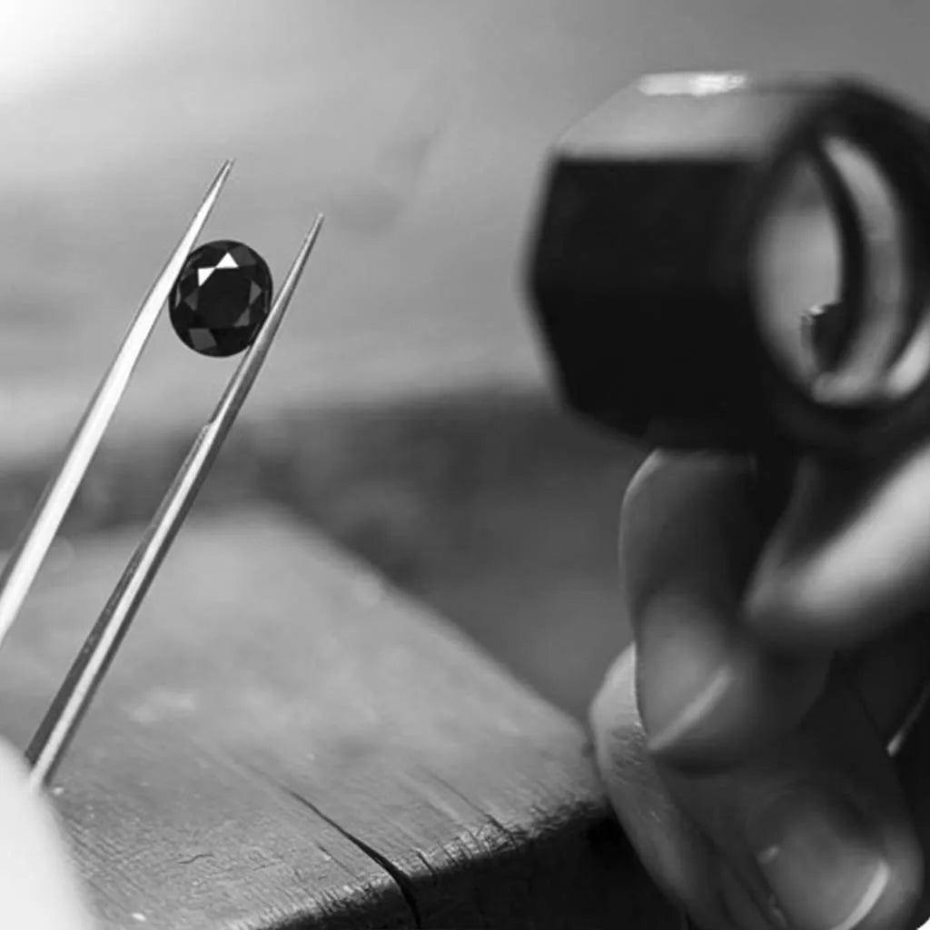 Diamante negro tallado sostenido por una pinza de gemologo con lupa de inspección al fondo